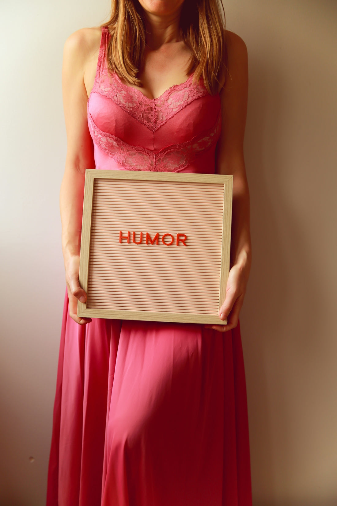 Woman in pink dress holds a board with humor.